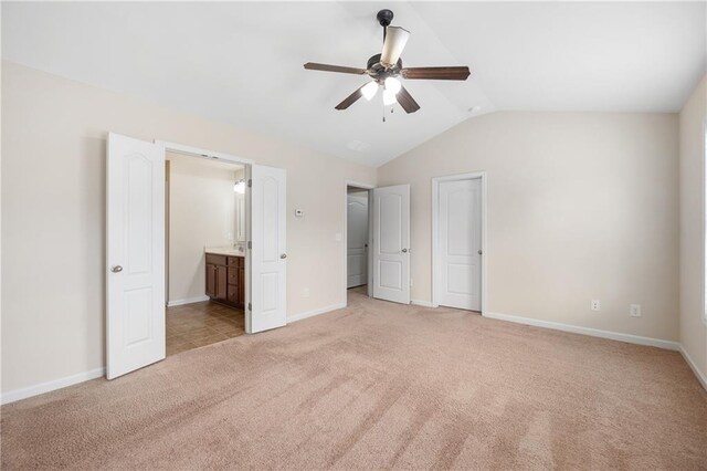 unfurnished bedroom featuring ceiling fan, light colored carpet, ensuite bathroom, and vaulted ceiling