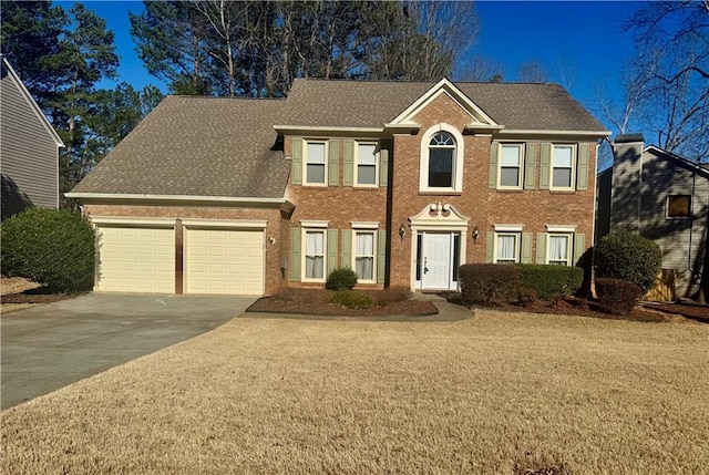 colonial inspired home with a garage, brick siding, concrete driveway, and roof with shingles