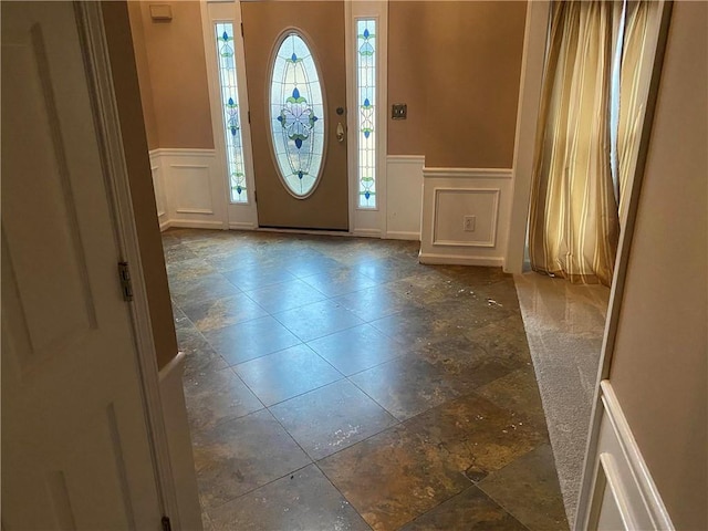 entryway featuring a wainscoted wall, stone tile floors, and a decorative wall