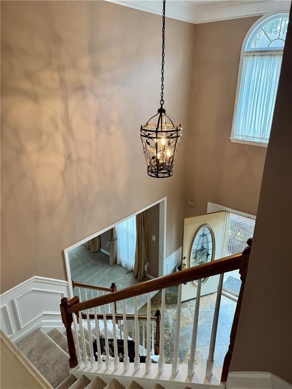 stairway featuring a chandelier, ornamental molding, wainscoting, and a decorative wall