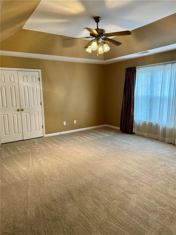 empty room featuring a tray ceiling, visible vents, a ceiling fan, carpet flooring, and baseboards