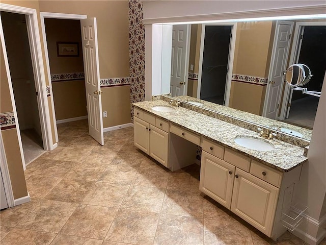 full bathroom with a walk in closet, a sink, baseboards, and double vanity