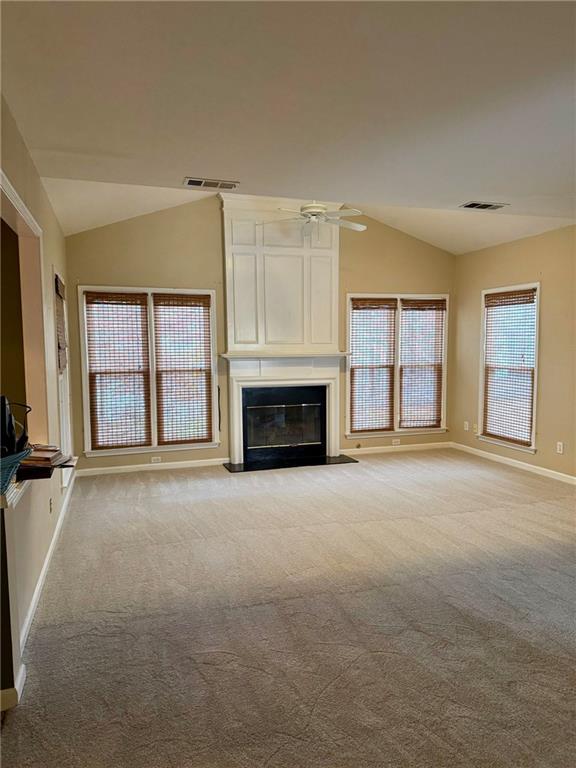 unfurnished living room with carpet, lofted ceiling, visible vents, a ceiling fan, and a glass covered fireplace