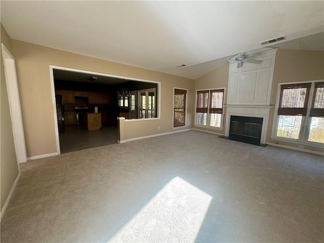 unfurnished living room with a large fireplace, vaulted ceiling, carpet, and visible vents