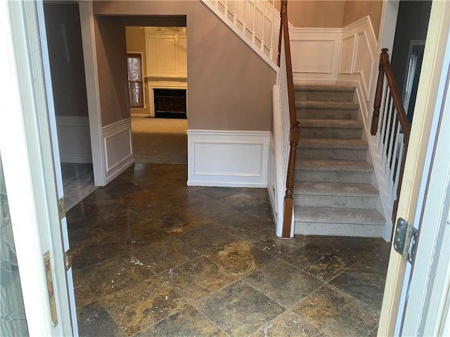 stairs with stone finish flooring, wainscoting, and a decorative wall