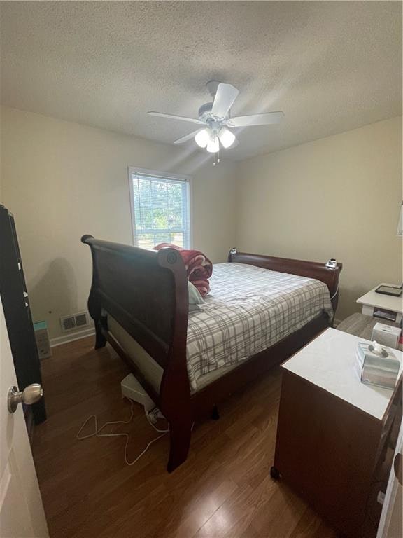 bedroom with ceiling fan, a textured ceiling, and dark wood-type flooring