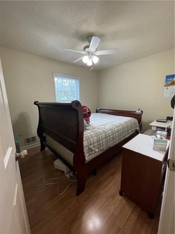 bedroom featuring ceiling fan, dark hardwood / wood-style flooring, and a textured ceiling