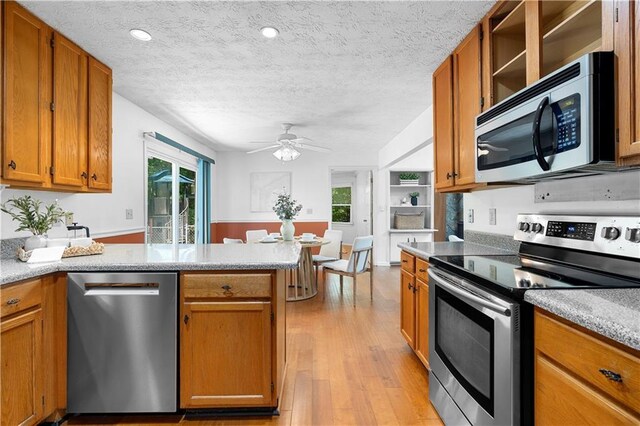 1920 Jett Ridge Rd, Cumming, GA 30041 - kitchen with stainless steel appliances, a peninsula, brown cabinets, light wood-style floors, and open shelves