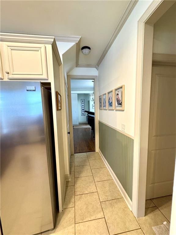 corridor featuring ornamental molding, light tile patterned floors, and wainscoting