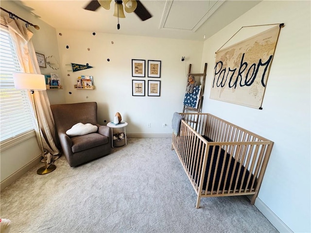 carpeted bedroom with attic access, a nursery area, baseboards, and ceiling fan