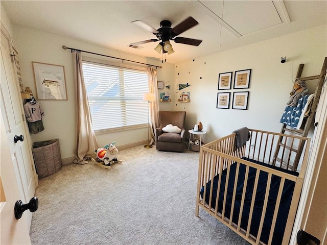 carpeted bedroom featuring visible vents, a crib, baseboards, attic access, and a ceiling fan