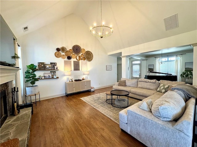 living room with visible vents, a fireplace with raised hearth, wood finished floors, a notable chandelier, and high vaulted ceiling