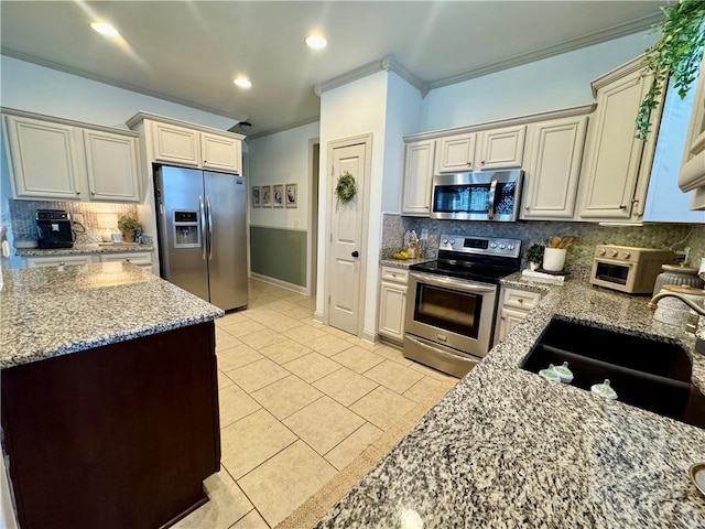 kitchen with ornamental molding, light stone counters, light tile patterned flooring, stainless steel appliances, and a sink