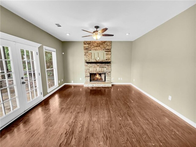 unfurnished living room with french doors, ceiling fan, a stone fireplace, and hardwood / wood-style floors