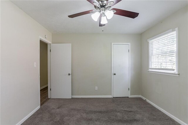 unfurnished bedroom with ceiling fan and dark carpet