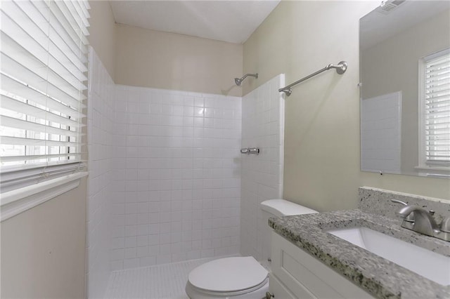 bathroom featuring a tile shower, vanity, and toilet