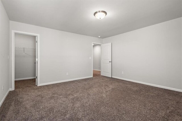 unfurnished bedroom with a spacious closet, a closet, and dark colored carpet