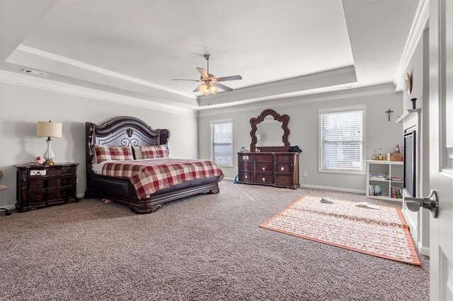 carpeted bedroom featuring a tray ceiling, ceiling fan, a fireplace, and ornamental molding