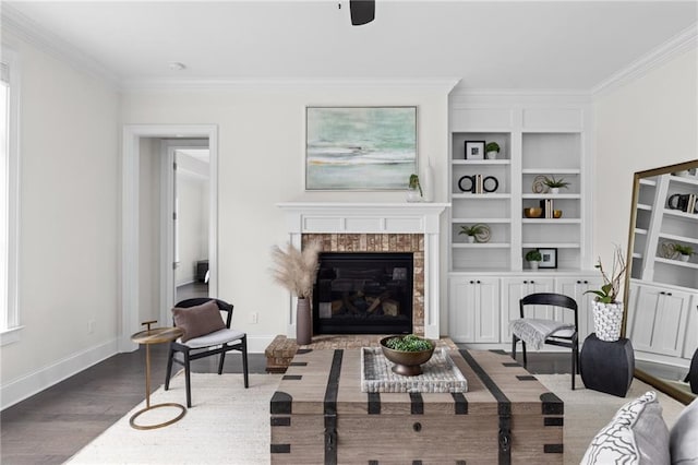 living area with ornamental molding, a glass covered fireplace, baseboards, and wood finished floors