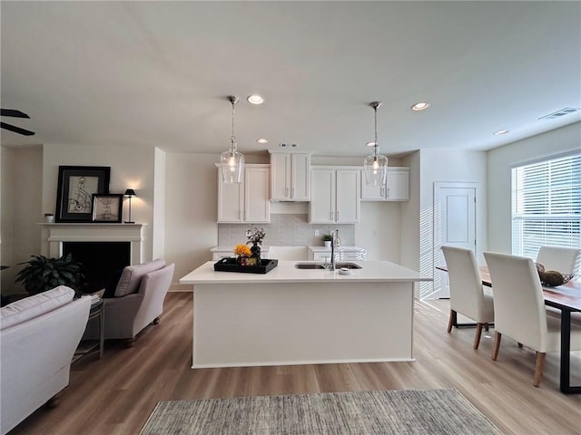 kitchen featuring tasteful backsplash, a kitchen island with sink, sink, pendant lighting, and white cabinetry