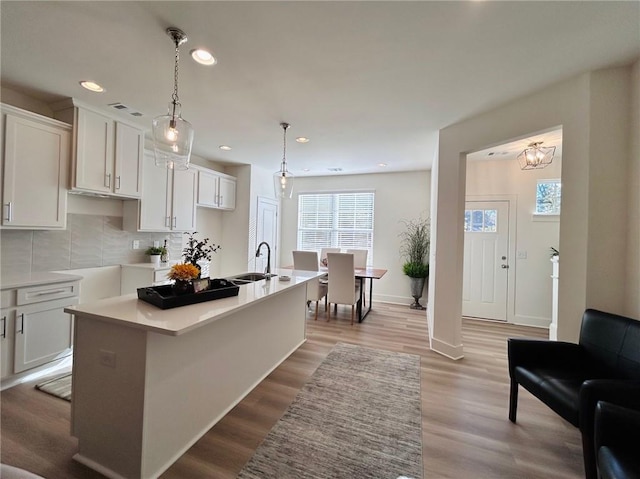 kitchen with a kitchen island with sink, white cabinets, sink, hanging light fixtures, and decorative backsplash