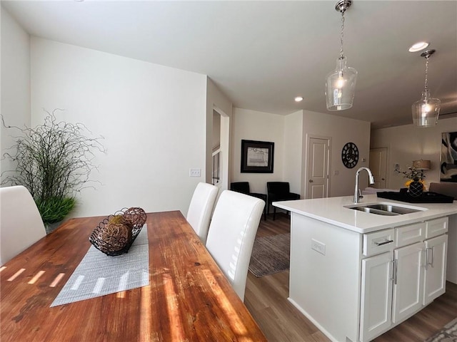 kitchen with sink, hardwood / wood-style flooring, white cabinetry, hanging light fixtures, and an island with sink