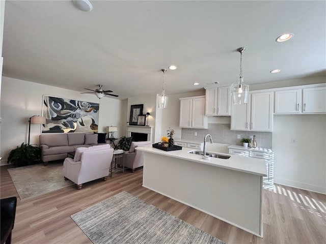 kitchen with sink, an island with sink, tasteful backsplash, decorative light fixtures, and white cabinetry