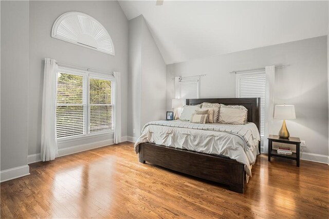 bedroom featuring wood finished floors, baseboards, and high vaulted ceiling