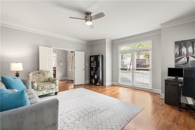 living room featuring ceiling fan, crown molding, baseboards, and wood finished floors