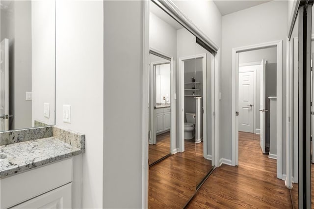 bathroom featuring baseboards, toilet, wood finished floors, and vanity