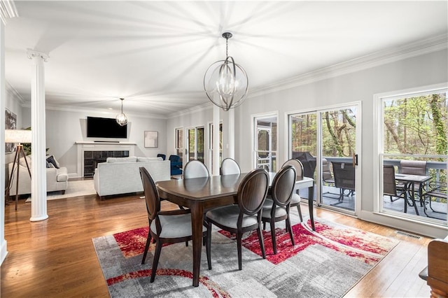 dining area with visible vents, ornamental molding, decorative columns, a tile fireplace, and wood finished floors