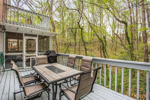 wooden terrace featuring outdoor dining area, a sunroom, and a grill