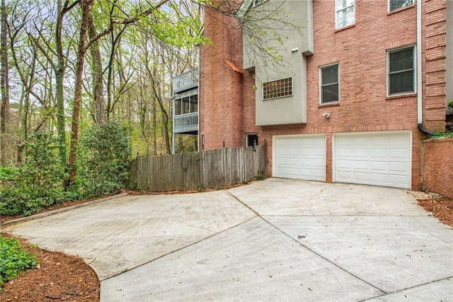 exterior space featuring brick siding, driveway, an attached garage, and fence