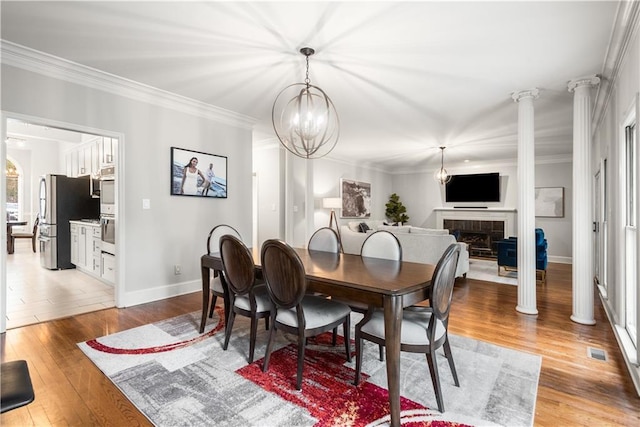 dining space with a tiled fireplace, light wood-style floors, visible vents, and ornamental molding