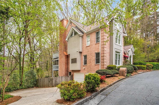 view of side of home with brick siding, fence, stucco siding, a chimney, and driveway