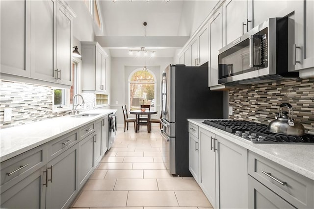 kitchen with a sink, an inviting chandelier, appliances with stainless steel finishes, light tile patterned floors, and a healthy amount of sunlight