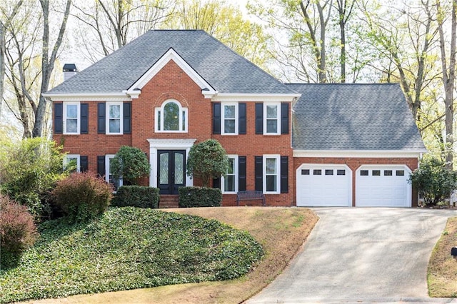 colonial house featuring french doors, a chimney, brick siding, concrete driveway, and an attached garage