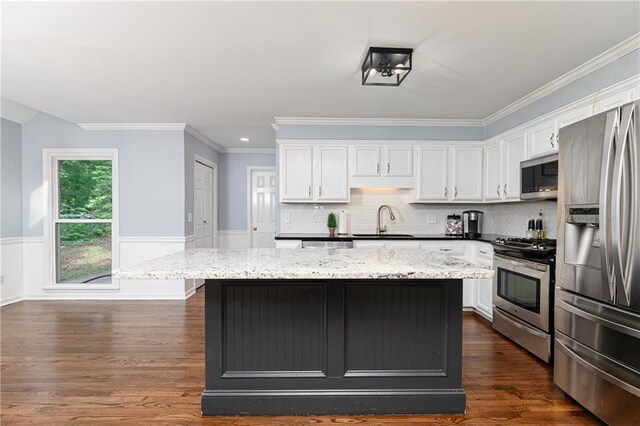 kitchen featuring white cabinets, wainscoting, a sink, a center island, and stainless steel appliances