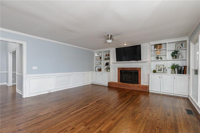 unfurnished living room with a brick fireplace, a ceiling fan, built in shelves, and ornamental molding