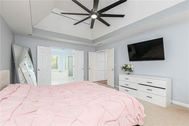 bedroom featuring light carpet, a raised ceiling, ensuite bath, a ceiling fan, and baseboards