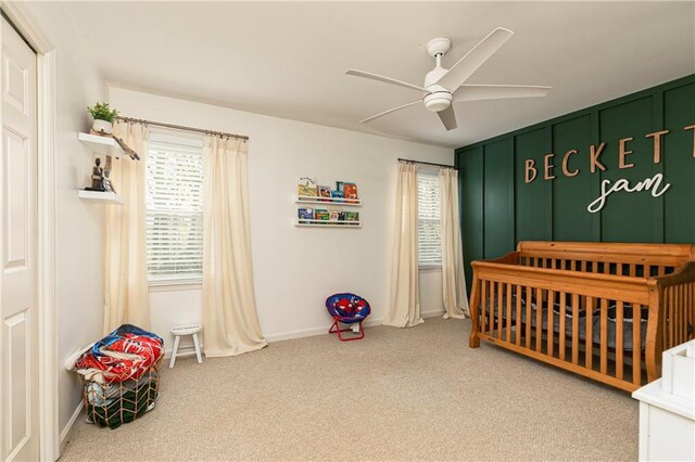 carpeted bedroom featuring a crib, baseboards, and a ceiling fan