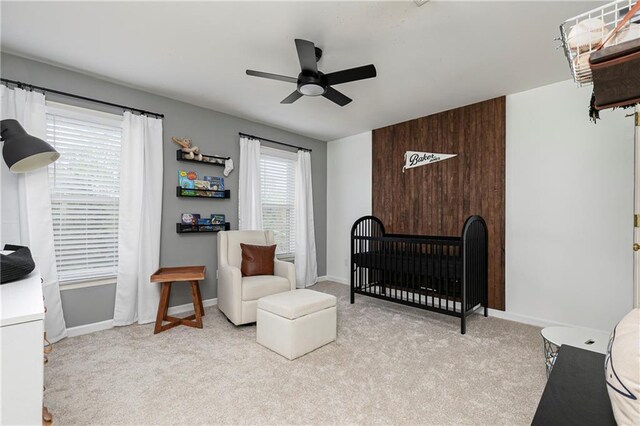 carpeted bedroom featuring baseboards, a crib, and ceiling fan