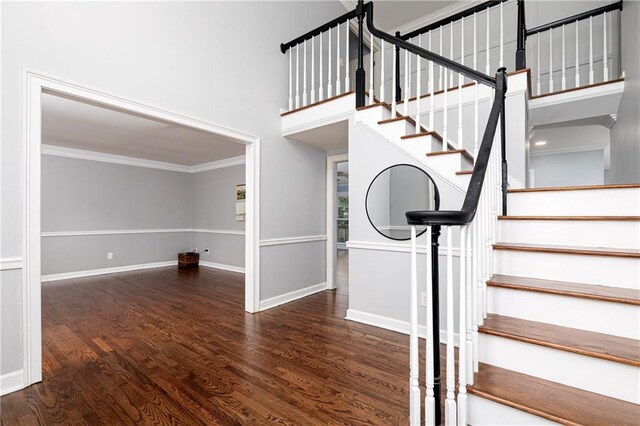 stairs featuring baseboards, ornamental molding, wood finished floors, and a towering ceiling
