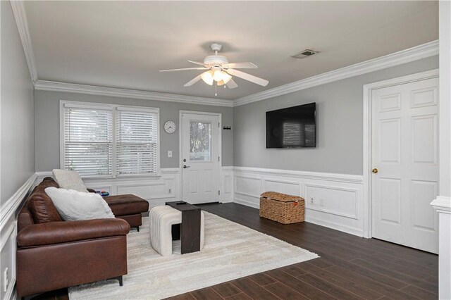 living room with crown molding, wainscoting, a ceiling fan, dark wood-type flooring, and visible vents