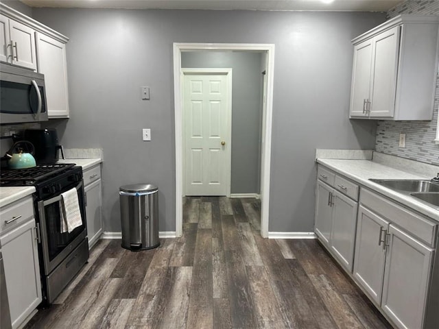 kitchen with a sink, dark wood-style flooring, backsplash, light countertops, and appliances with stainless steel finishes
