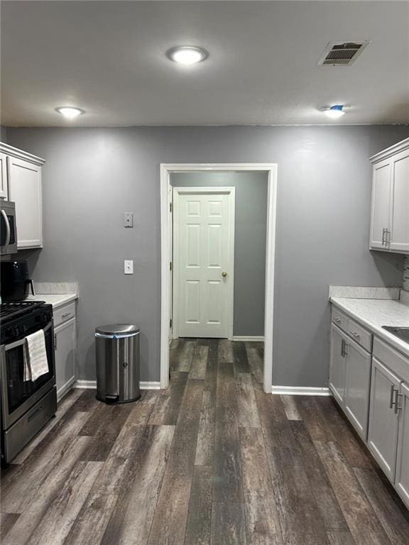 kitchen with dark wood finished floors, black electric range oven, light countertops, stainless steel microwave, and visible vents