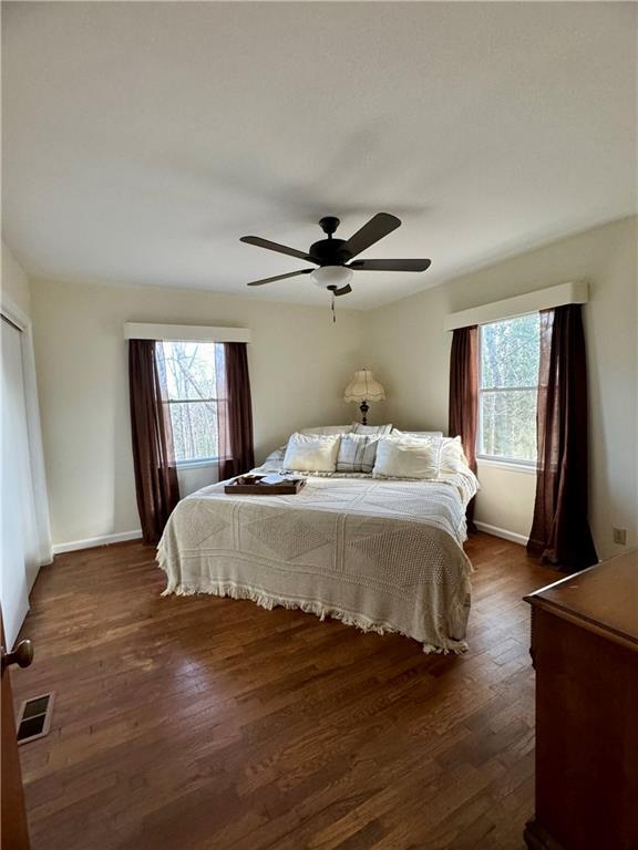 bedroom with baseboards, multiple windows, visible vents, and dark wood-type flooring