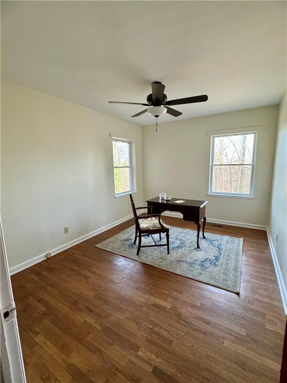 office space featuring a ceiling fan, baseboards, visible vents, and dark wood-type flooring