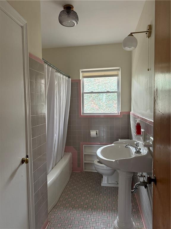 full bath featuring tile walls, tile patterned floors, a wainscoted wall, toilet, and shower / bathtub combination with curtain