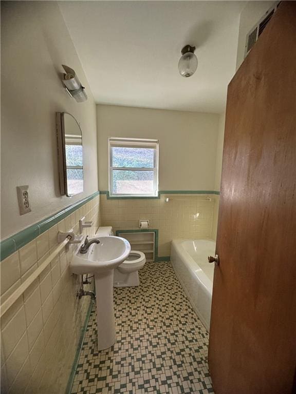 full bath with a bath, tile walls, a wainscoted wall, tile patterned floors, and toilet
